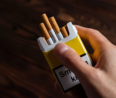 A mans hand holding out an open pack of cigarettes.