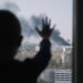 Silhouette of small child. Kid stands with his palms on the window and looks at the fire in city. Black smoke rises into the sky above high-rise buildings. Boy is worried. Child safety.