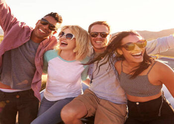Friends On Road Trip Sitting On Hood Of Convertible Car