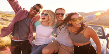 Friends On Road Trip Sitting On Hood Of Convertible Car