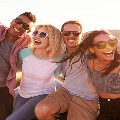 Friends On Road Trip Sitting On Hood Of Convertible Car