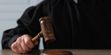 Judge with gavel sitting at wooden table, closeup