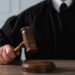 Judge with gavel sitting at wooden table, closeup