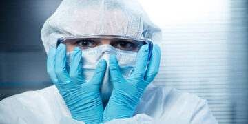 Terrified scientist head in hands wearing hazmat protective suit.