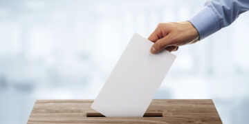 Ballot box with person casting vote on blank voting slip