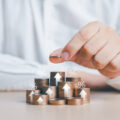Saving money concept. Businessman hand putting a coin on top of stacked growing coins with percentage and arrow up icons. Future plan and financial management idea. Income managing, money planning.