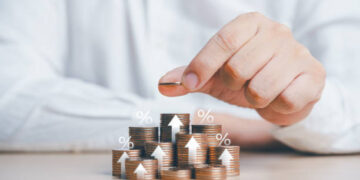 Saving money concept. Businessman hand putting a coin on top of stacked growing coins with percentage and arrow up icons. Future plan and financial management idea. Income managing, money planning.