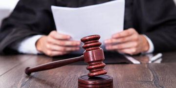 Close-up Of Male Judge In Front Of Mallet Holding Documents