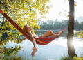 Woman relaxing on hammock by the river at sunset.