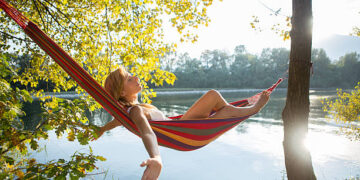 Woman relaxing on hammock by the river at sunset.