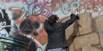 Young man spraypaints name on graffiti wall