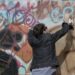 Young man spraypaints name on graffiti wall