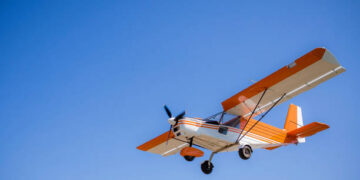 light single private orange plane in clear blue sky