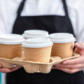 Waiter barista holding and serving take out a paper disposable cup of hot coffee in cafe
