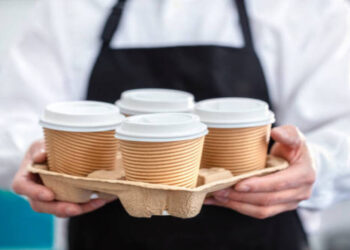 Waiter barista holding and serving take out a paper disposable cup of hot coffee in cafe