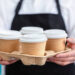 Waiter barista holding and serving take out a paper disposable cup of hot coffee in cafe