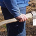 one male worker in blue clothes holds a gray ax in his hand on the street