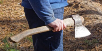 one male worker in blue clothes holds a gray ax in his hand on the street