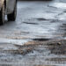 Close-up of potholes on a wet urban road with a passing vehicle, illustrating damaged infrastructure, poor road conditions, traffic safety risks, and the need for road maintenance in city environments.