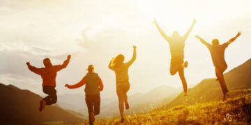 Group of five happy friends is running and jumping in sunset light on background of mountains. Happiness and friendship concept