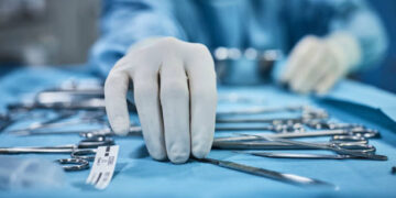 Surgeon picking up surgical tool from tray. Surgeon is preparing for surgery in operating room. He is in a hospital.