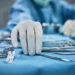 Surgeon picking up surgical tool from tray. Surgeon is preparing for surgery in operating room. He is in a hospital.