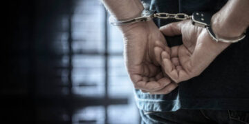 Arrested man in handcuffs with handcuffed hands behind back in prison