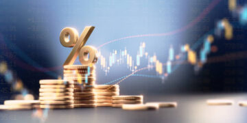 Percentage sign on top of coin stacks before blue financial graph. Horizontal composition with copy space. Business and finance concept.