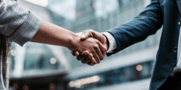Meeting success. Two business persons shaking hands standing outside